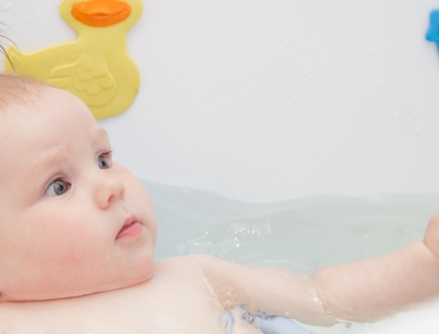 bathing a baby in a bath with a yellow rubber duck in picture